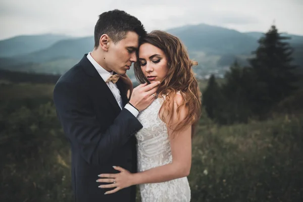 Joven pareja recién casada, novia y novio besándose, abrazándose a la vista perfecta de las montañas, cielo azul — Foto de Stock