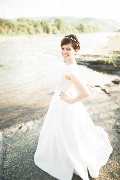 Splendida bella sposa sorride mentre posa sul fiume con bouquet — Foto Stock