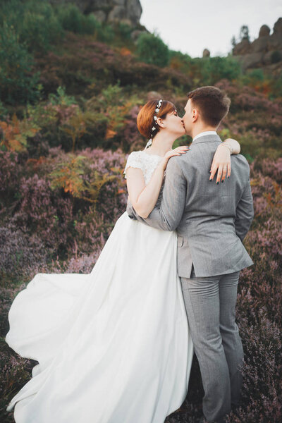 Gorgeous wedding couple kissing and hugging in forest with big rocks.
