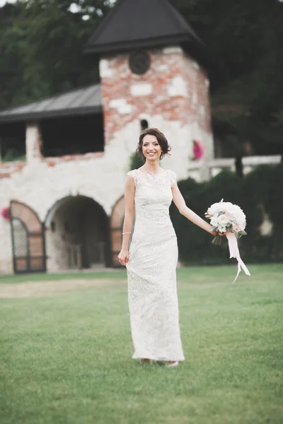 Hermosa novia en elegante vestido blanco sosteniendo ramo posando en el parque — Foto de Stock