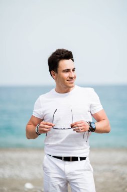 Sahilde gülümseyen güneş gözlüklü genç yakışıklı adam portresi