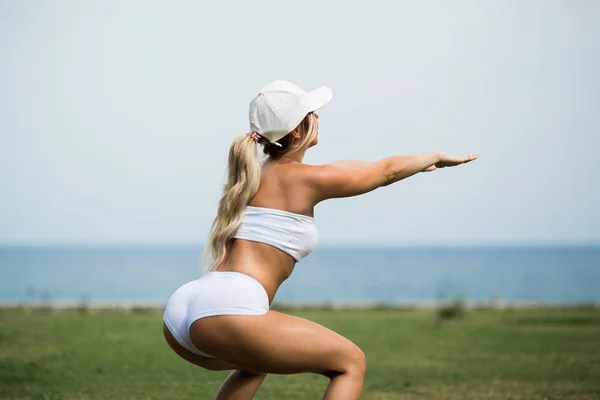 Beautiful girl is working out in summer park with a view on the sea — Stock Photo, Image