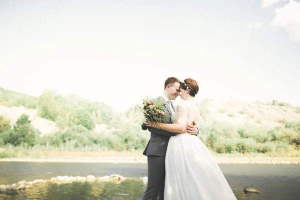 Bride and groom holding beautiful wedding bouquet. Posing near river — Stock Photo, Image