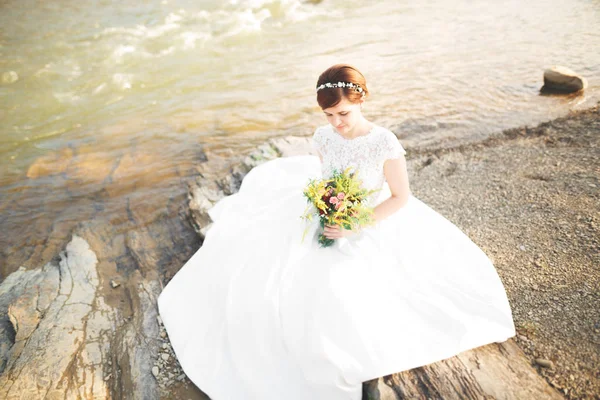 Nádherná nevěsta krásné úsměvy při pózování u řeky s kyticí — Stock fotografie