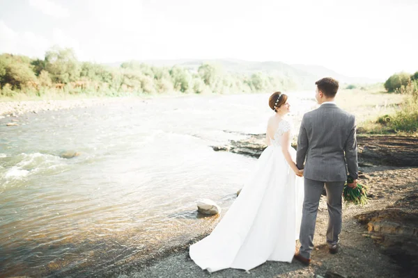 Novia y novio celebrando hermoso ramo de bodas. Posando cerca del río — Foto de Stock