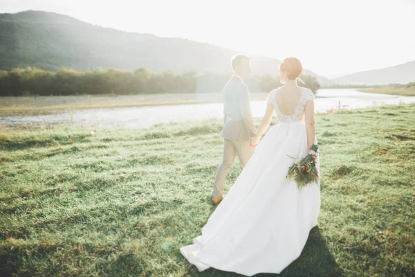 Yeni evli çift, gelin ve damat öpüşüyor, mükemmel dağ manzarasında sarılıyorlar, mavi gökyüzü