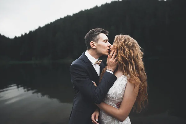 Joven pareja recién casada, novia y novio besándose, abrazándose a la vista perfecta de las montañas, cielo azul — Foto de Stock