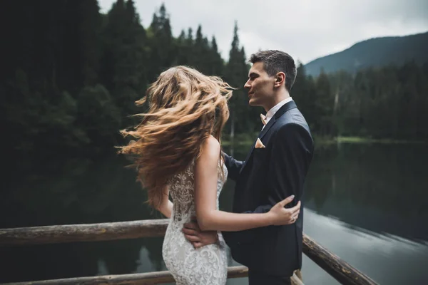 Young newly wed couple, bride and groom kissing, hugging on perfect view of mountains, blue sky — Stock Photo, Image