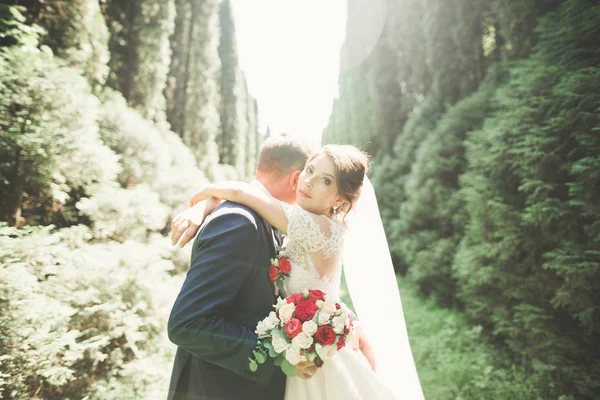 Stilvolles Brautpaar spaziert am Hochzeitstag mit Blumenstrauß durch den Park — Stockfoto