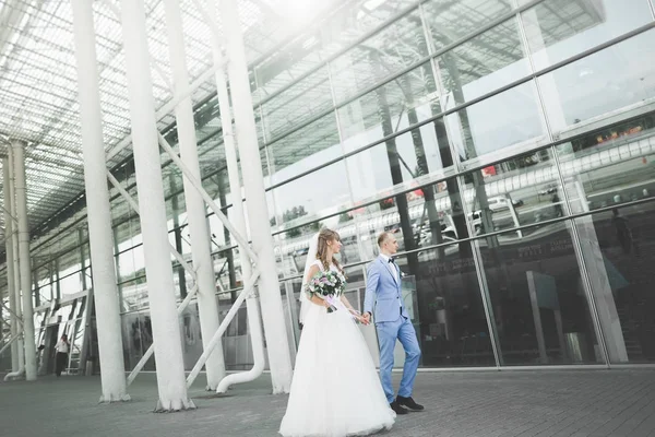 Lovely happy wedding couple, bride with long white dress posing near modern building — Stock Photo, Image