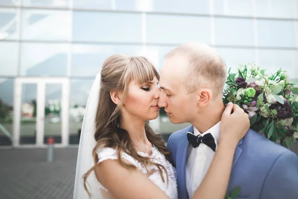 Lovely happy wedding couple, bride with long white dress posing near modern building — Stock Photo, Image