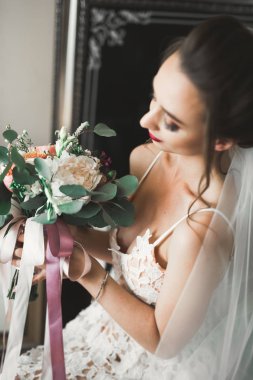 Cüppeli muhteşem gelin bir odada düğün töreni için poz veriyor ve hazırlanıyor.