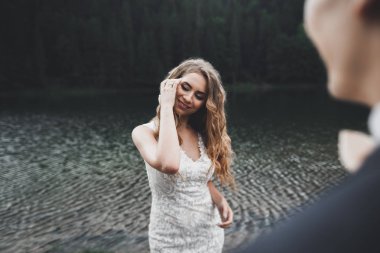 Yeni evli çift, gelin ve damat öpüşüyor, mükemmel dağ manzarasında sarılıyorlar, mavi gökyüzü