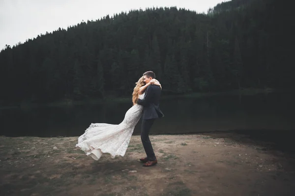 Joven pareja recién casada, novia y novio besándose, abrazándose a la vista perfecta de las montañas, cielo azul —  Fotos de Stock