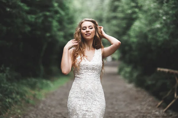 Bela noiva em elegante vestido branco segurando buquê posando no parque — Fotografia de Stock