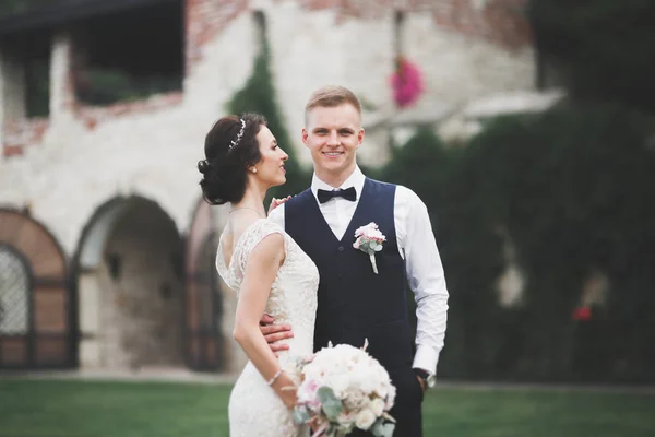 Elegante coppia di sposi felici che passeggiano nel parco il giorno del loro matrimonio con bouquet — Foto Stock