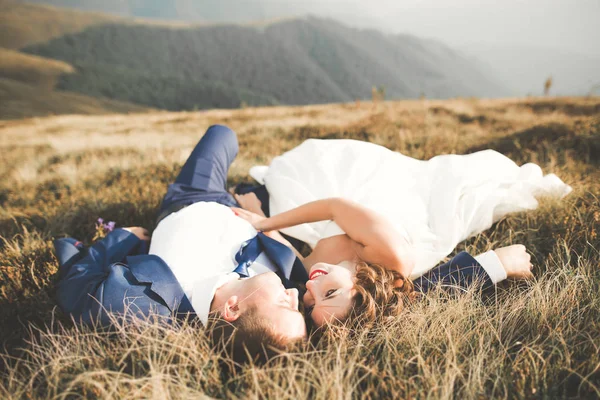 Νεαρό νιόπαντρο ζευγάρι, νύφη και γαμπρός φιλιούνται, αγκαλιάζονται από την τέλεια θέα των βουνών, γαλάζιο ουρανό — Φωτογραφία Αρχείου