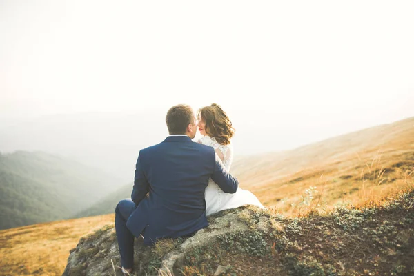 Hermosa pareja de boda posando en la cima de una montaña al atardecer — Foto de Stock