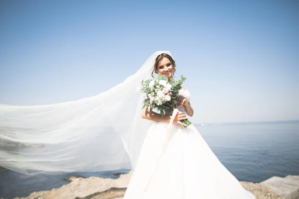 Schöne junge Braut mit Brautstrauß posiert auf dem Hintergrund Meer — Stockfoto