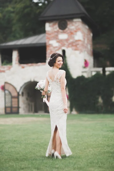 Schöne brünette Braut im eleganten weißen Kleid mit Strauß posiert ordentlich Bäume — Stockfoto