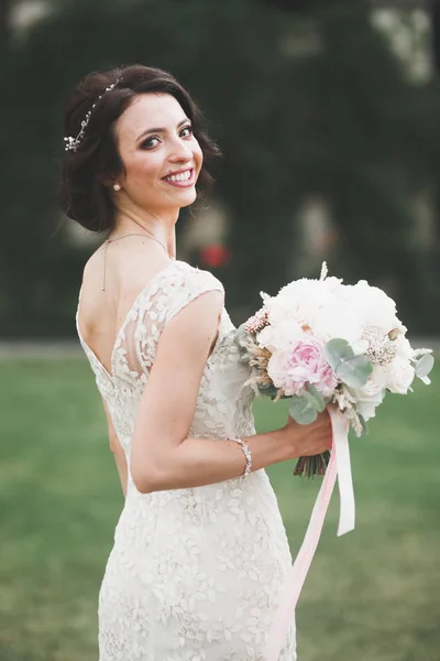 Красива брюнетка наречена в елегантній білій сукні тримає букет позує акуратні дерева — стокове фото