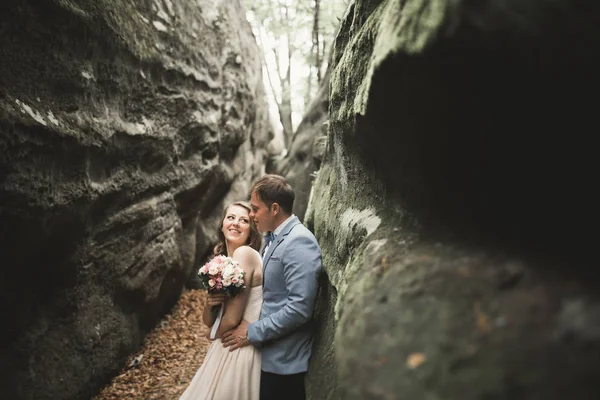 Hermosa pareja de boda besándose y abrazándose en el bosque con grandes rocas — Foto de Stock