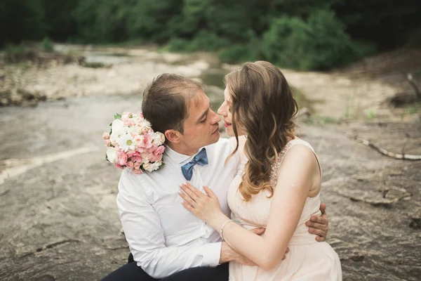 Elegante novio elegante y elegante novia cerca del río con piedras. Pareja de boda enamorada — Foto de Stock