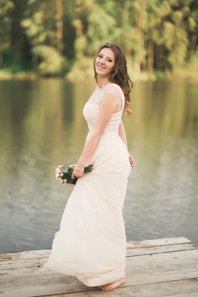 抱着花束附近森林和湖泊构成的优雅穿着华丽的新娘 — 图库照片