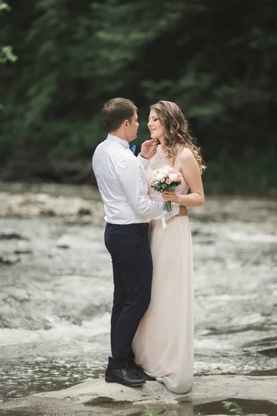 Zarif nazik şık damat ve gelin taşlarla Nehri yakınında. Evlilik çift aşık — Stok fotoğraf