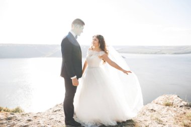 Şık, şık, mutlu bir düğün çifti, gelin, deniz ve gökyüzünün arka planında muhteşem bir damat.