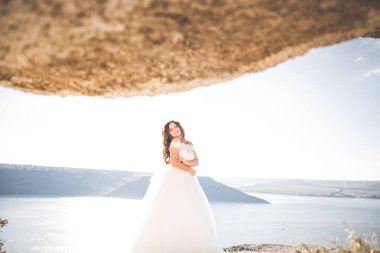 Güzel bayan, gelin gün batımında deniz kenarında bir gelinlik içinde poz veriyor.