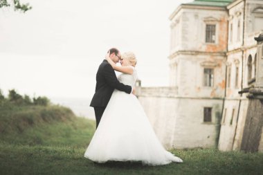 Güzel, romantik bir düğün. Yeni evliler. Eski kalenin yakınlarında sarılıyorlar.