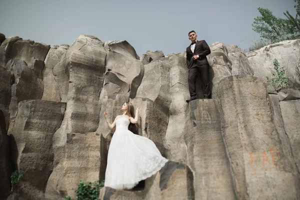 Birbirlerine aşık düğün çifti güzel manzarada kayaların yanında öpüşüyor ve sarılıyorlar. — Stok fotoğraf