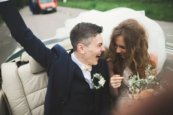 Stijlvol bruidspaar, bruid, bruidegom kussen en knuffelen op retro auto — Stockfoto