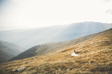 Yeni evli çift, gelin ve damat öpüşüyor, mükemmel dağ manzarasında sarılıyorlar, mavi gökyüzü