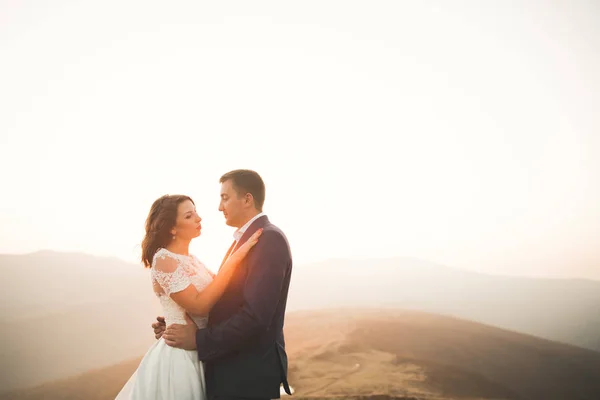 Giovane coppia appena sposata, sposa e sposo baciare, abbracciando sulla vista perfetta delle montagne, cielo blu — Foto Stock