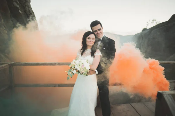 Ślub, para pozowanie w pobliżu skały z kolorowe dymu za nimi — Zdjęcie stockowe