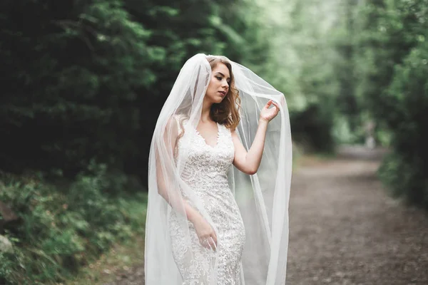 Schöne Braut im eleganten weißen Kleid mit Blumenstrauß posiert im Park — Stockfoto