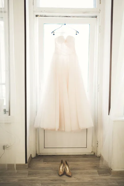 Fashion wedding dress for bride hanging near window — Stock Photo, Image