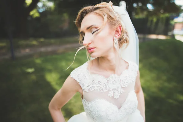 Bela noiva em elegante vestido branco segurando buquê posando no parque — Fotografia de Stock