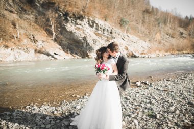 Düğün çifti, damat ve gelin kucaklaşıyor, nehir kenarında.