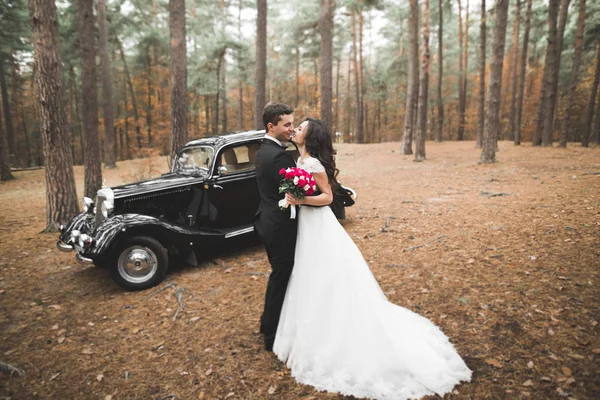 Stilvolles Hochzeitspaar, Braut, Bräutigam küssen und umarmen sich im Herbst in der Nähe von Retro-Autos — Stockfoto