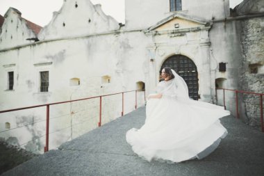 Zarif beyaz elbiseli güzel esmer gelin elinde buket ile güzel ağaçlar poz veriyor.