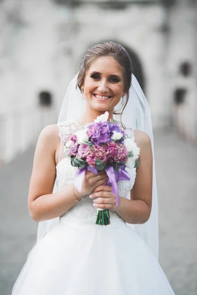 Bela noiva elegante com vestido de noiva perfeito e buquê posando perto do castelo velho — Fotografia de Stock