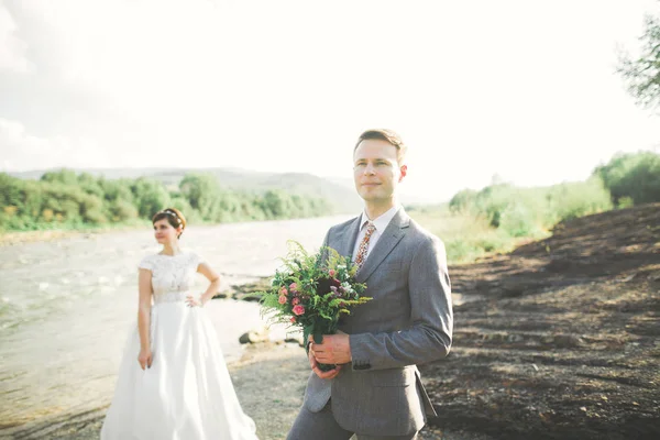 Schöner romantischer Bräutigam und schöne Braut posieren in Flussnähe in malerischen Bergen — Stockfoto