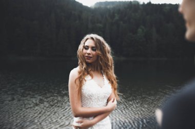 Yeni evli çift, gelin ve damat öpüşüyor, mükemmel dağ manzarasında sarılıyorlar, mavi gökyüzü