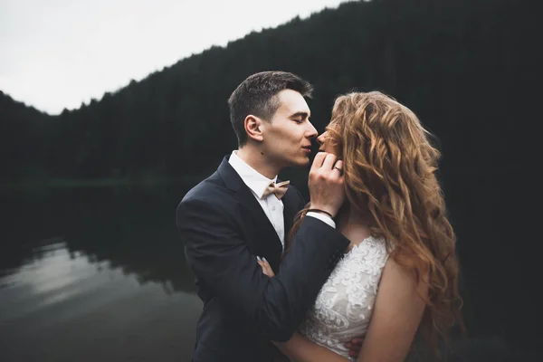 Hermosa pareja de boda besándose y abrazándose cerca de la montaña con vista perfecta —  Fotos de Stock