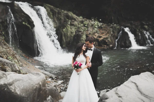 Vackra bröllop par kysser och omfamnar nära stranden av en bergsflod med stenar — Stockfoto
