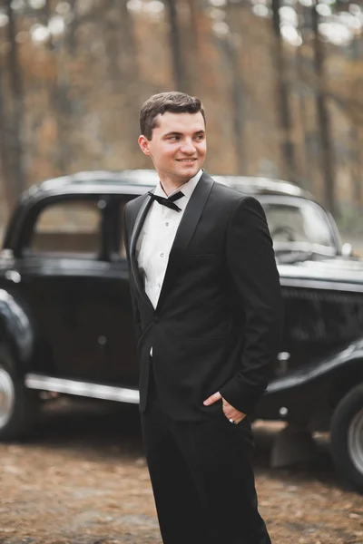 Красивий наречений на весіллі посміхається і чекає нареченої біля ретро-автомобіля — стокове фото