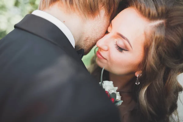 Stilvolles Brautpaar spaziert am Hochzeitstag mit Blumenstrauß durch den Park — Stockfoto